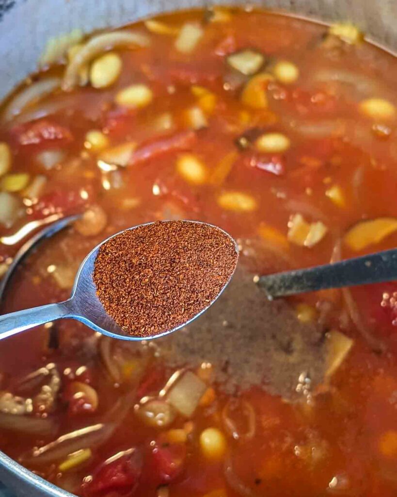 A spoonful of hot Hatch red chile powder about to go into a bowl of Minestrone soup